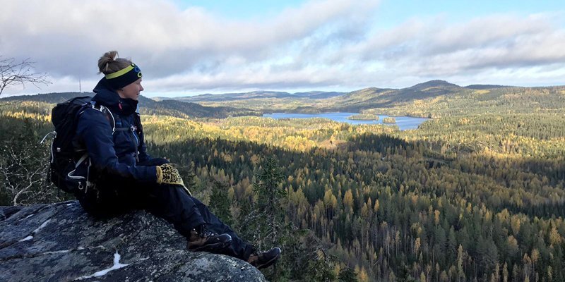 Eräopas Saana Lappalainen istuu rinkka selässä Kolilla korkealla kalliolla. Oikealle avautuu metsäinen maisema. 