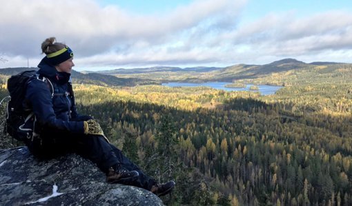Eräopas Saana Lappalainen istuu rinkka selässä Kolilla korkealla kalliolla. Oikealle avautuu metsäinen maisema. 