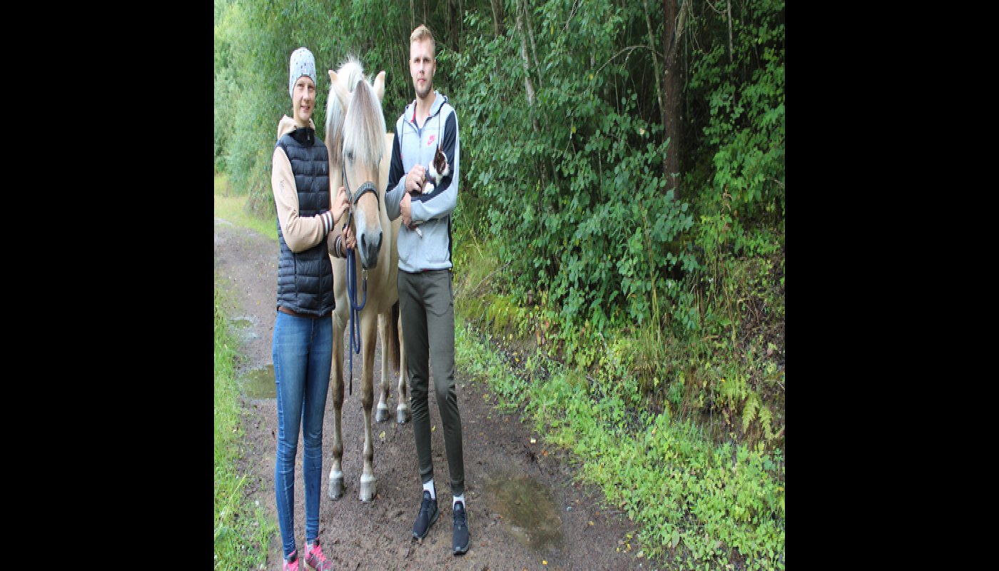 Salla ja Samu Jokela seisovat hevosen kanssa metsäpolulla. Ympärillä on rehevää kesäistä metsää.