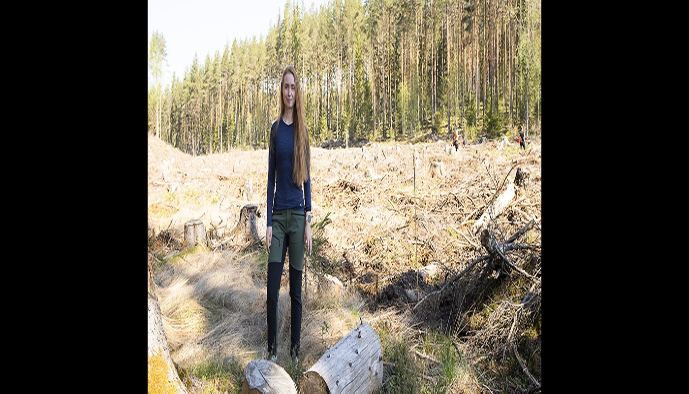 Inna Salminen seisoo hakkuuaukon reunalla. Taustalla kaksi henkilöä istuttaa puuntaimia.