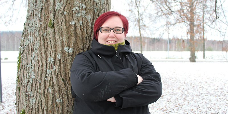 Hanna Parviainen seisoo kädet rinnalla ristissä puun edessä. Taustalla näkyy lumista maata ja puistopuita. 