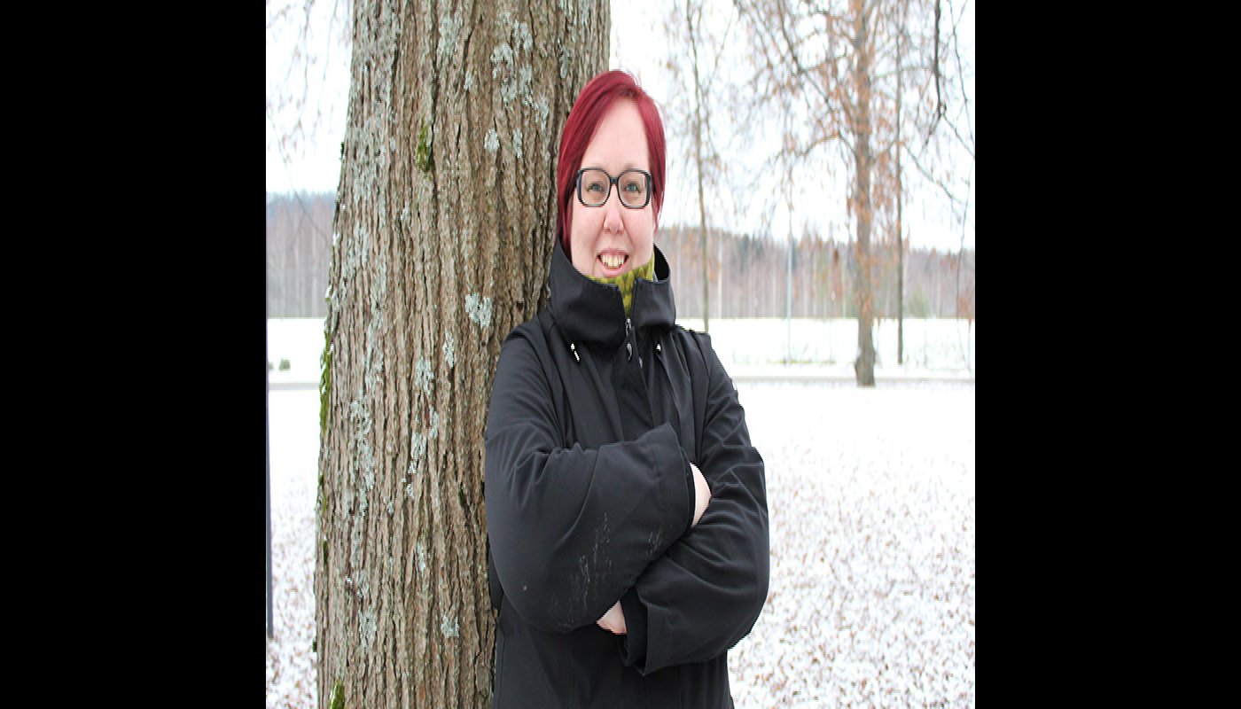 Hanna Parviainen seisoo kädet rinnalla ristissä puun edessä. Taustalla näkyy lumista maata ja puistopuita. 