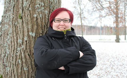 Hanna Parviainen seisoo kädet rinnalla ristissä puun edessä. Taustalla näkyy lumista maata ja puistopuita. 