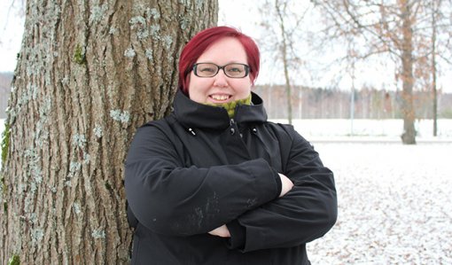 Hanna Parviainen seisoo kädet rinnalla ristissä puun edessä. Taustalla näkyy lumista maata ja puistopuita. 