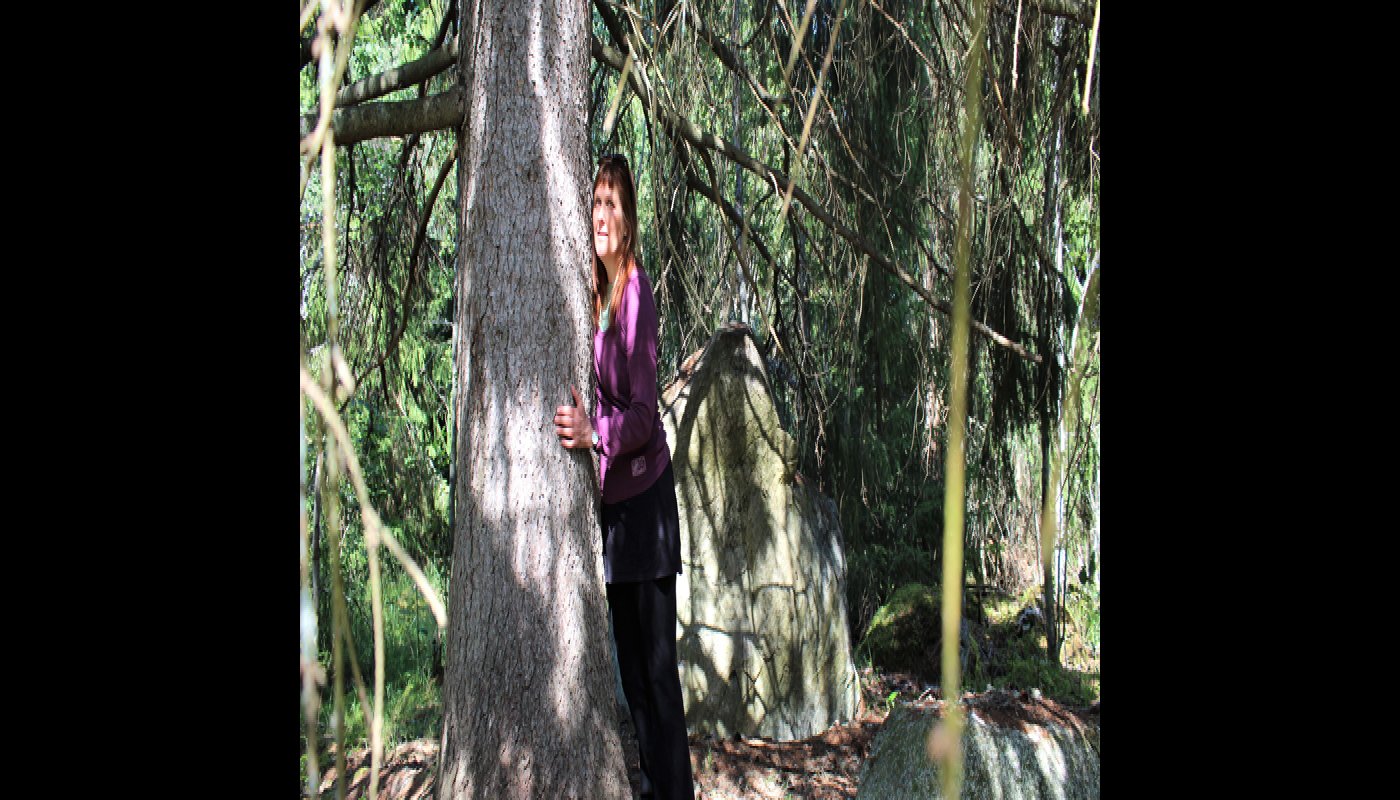 Kirsi Salonen nojaa paksurunkoiseen, vanhaan kuuseen. 