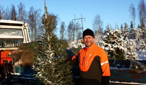 Antti Heikkilä joulukuusen kanssa talvella. Taustalla on pieni traktori ja sähkölinja.