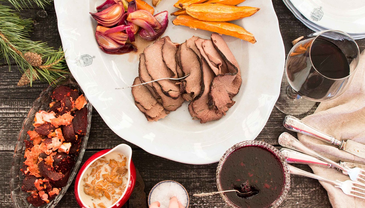 Jouluruokia katettuna pöytään. Lautasella on paistia, porkkanoita ja punasipuleita. Vieressä kulhossa rosollia ja kastiketta. Lasikulhossa on hyytelöä ja lasissa punaista juomaa.