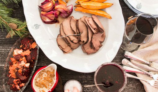 Jouluruokia katettuna pöytään. Lautasella on paistia, porkkanoita ja punasipuleita. Vieressä kulhossa rosollia ja kastiketta. Lasikulhossa on hyytelöä ja lasissa punaista juomaa.