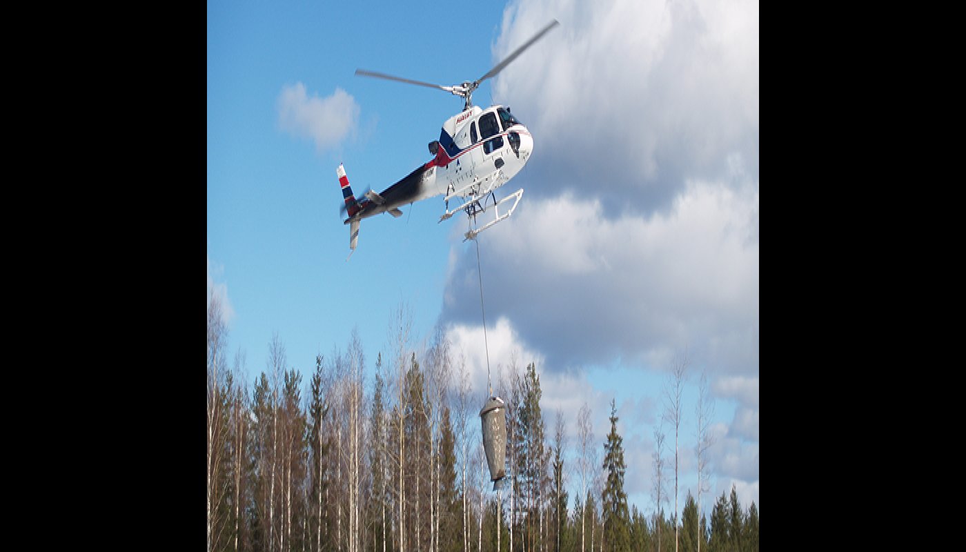 Helikopteri levittää tuhkalannoitetta metsään. 