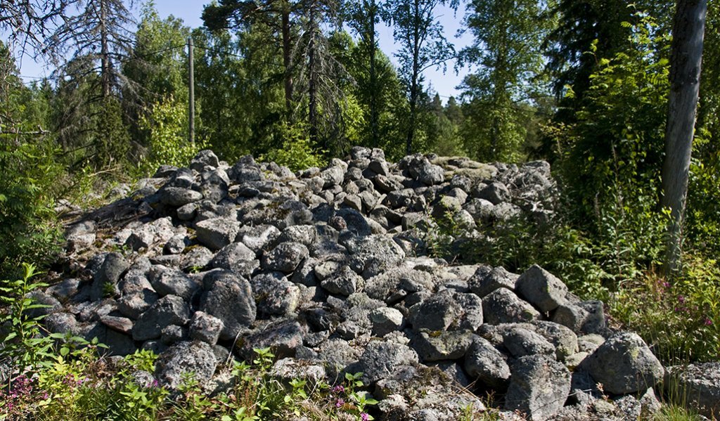 Kuvassa on muinainen hautaröykkiö, jossa on isoja kivenlohkareita. 