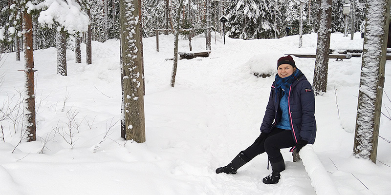 Anni Pylvänäinen istuu puulla talvisessa puistometsässä.