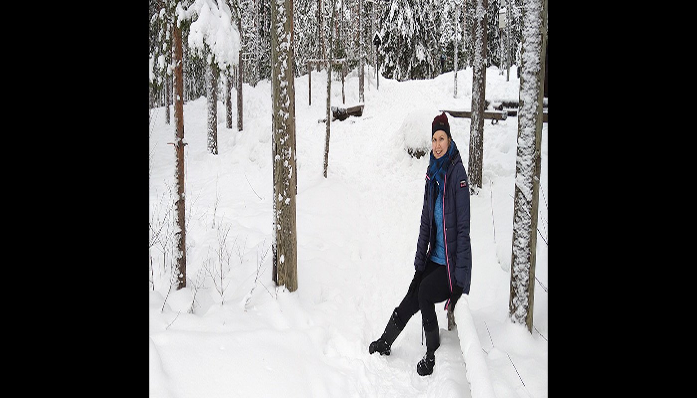 Anni Pylvänäinen istuu puulla talvisessa puistometsässä.