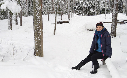 Anni Pylvänäinen istuu puulla talvisessa puistometsässä.