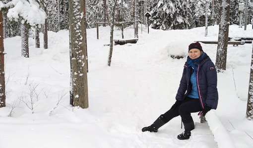 Anni Pylvänäinen istuu puulla talvisessa puistometsässä.