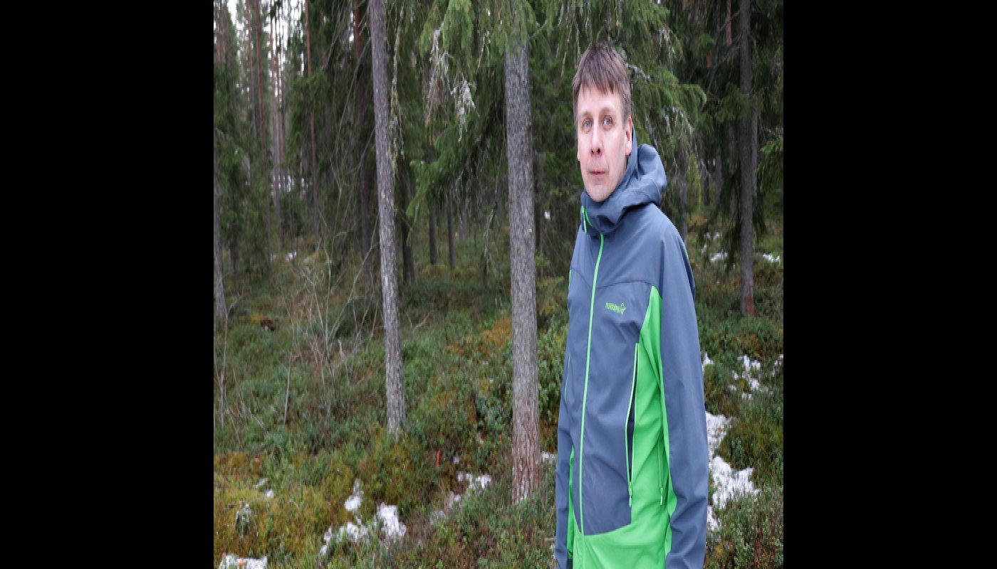 Rami Mattila seisoo omassa metsässään. Taustalla on kuusia ja varvikkoa sekä maassa on hieman lunta. 
