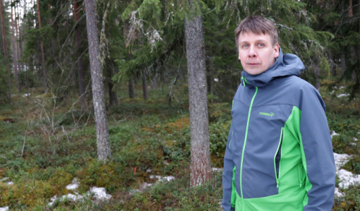 Rami Mattila seisoo omassa metsässään. Taustalla on kuusia ja varvikkoa sekä maassa on hieman lunta.
