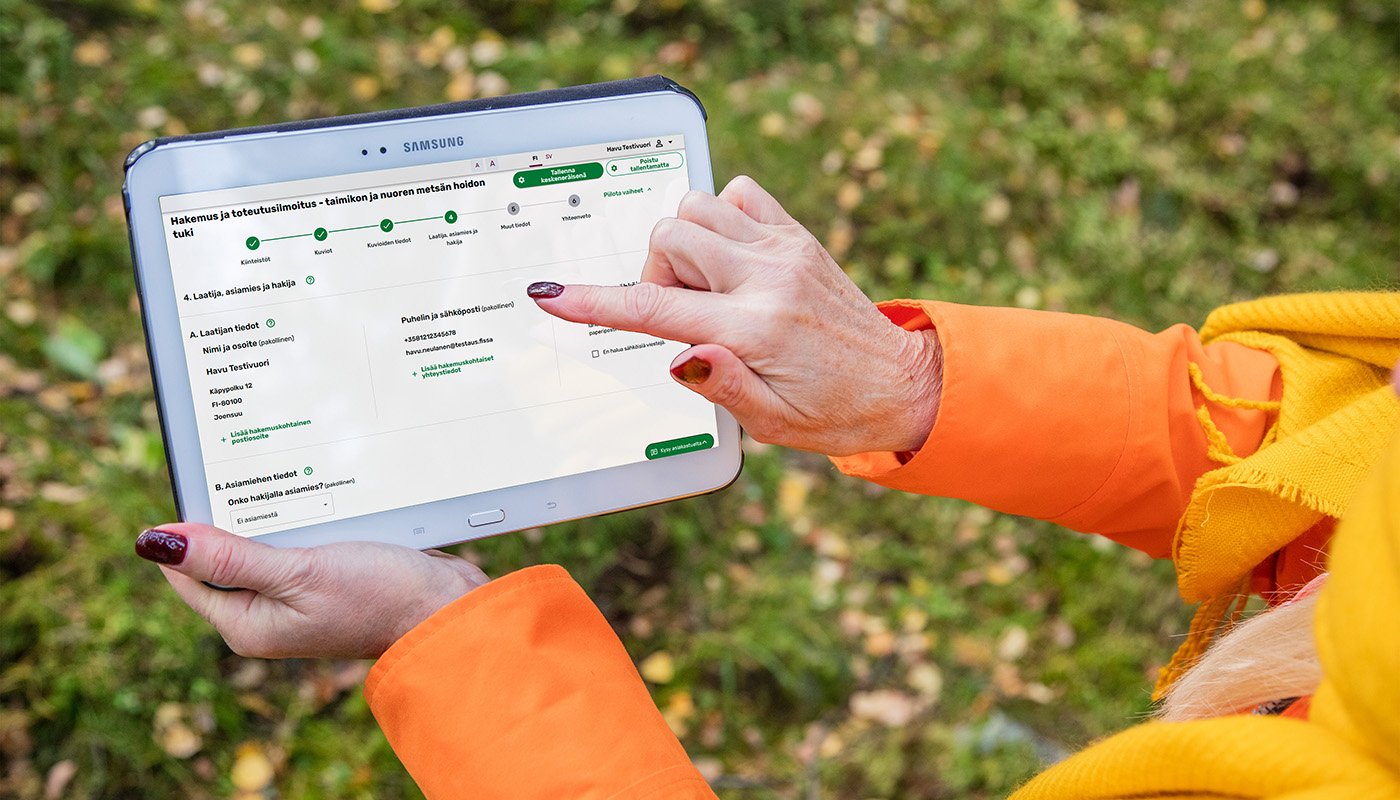 Henkilö osoittaa sormella tablettia, jossa on avoinna Metsään.fi-palvelu