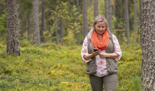 Nainen kävelee metsässä puhelimen kanssa.