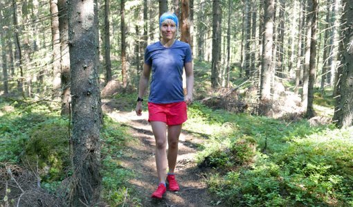 Saara Grönholm kävelee eteenpäin polulla ja hymyilee. Ympärillä on kuusimetsää ja varvikkoa.