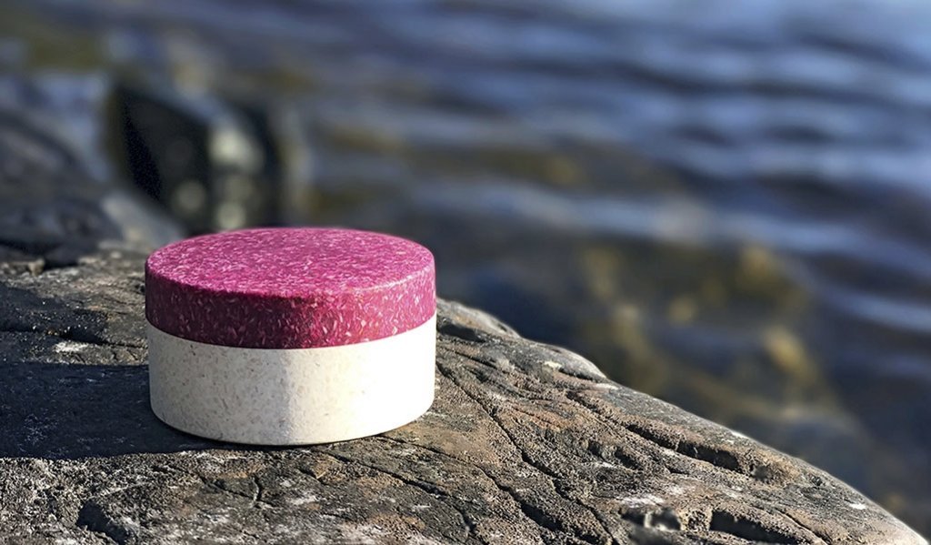 Sulapacin mikromuoviton ja puupohjainen pakkaus kuvattuna kiven päällä veden äärellä. 