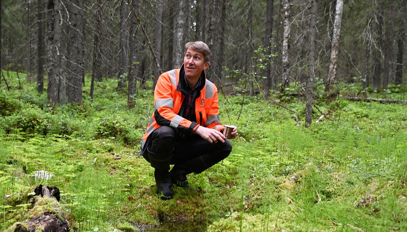 Jussi Vatanen on kyykistyneenä metsässä olevan lähteen vieressä. 