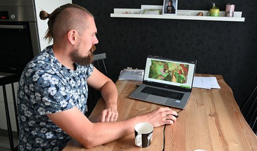 Tuomas Vakkila katsoo keittiön pöydän ääressä kannettavalta tietokoneelta Metsään.fi-palvelua ja oman metsänsä tietoja. 