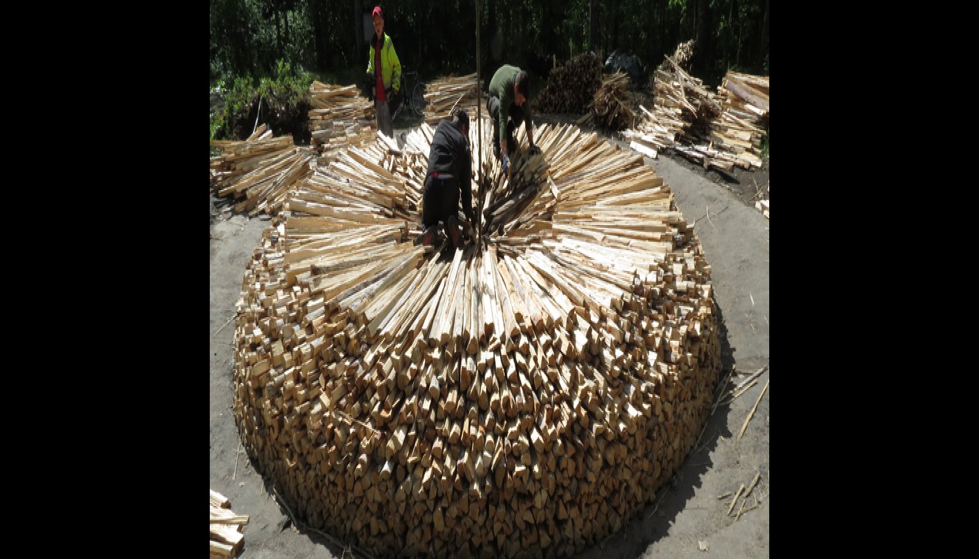 Kuvassa kaksi miestä latoo puita pyöreään muodostelmaan tervahautaan. Yksi mies seuraa ladontaa vierestä. 