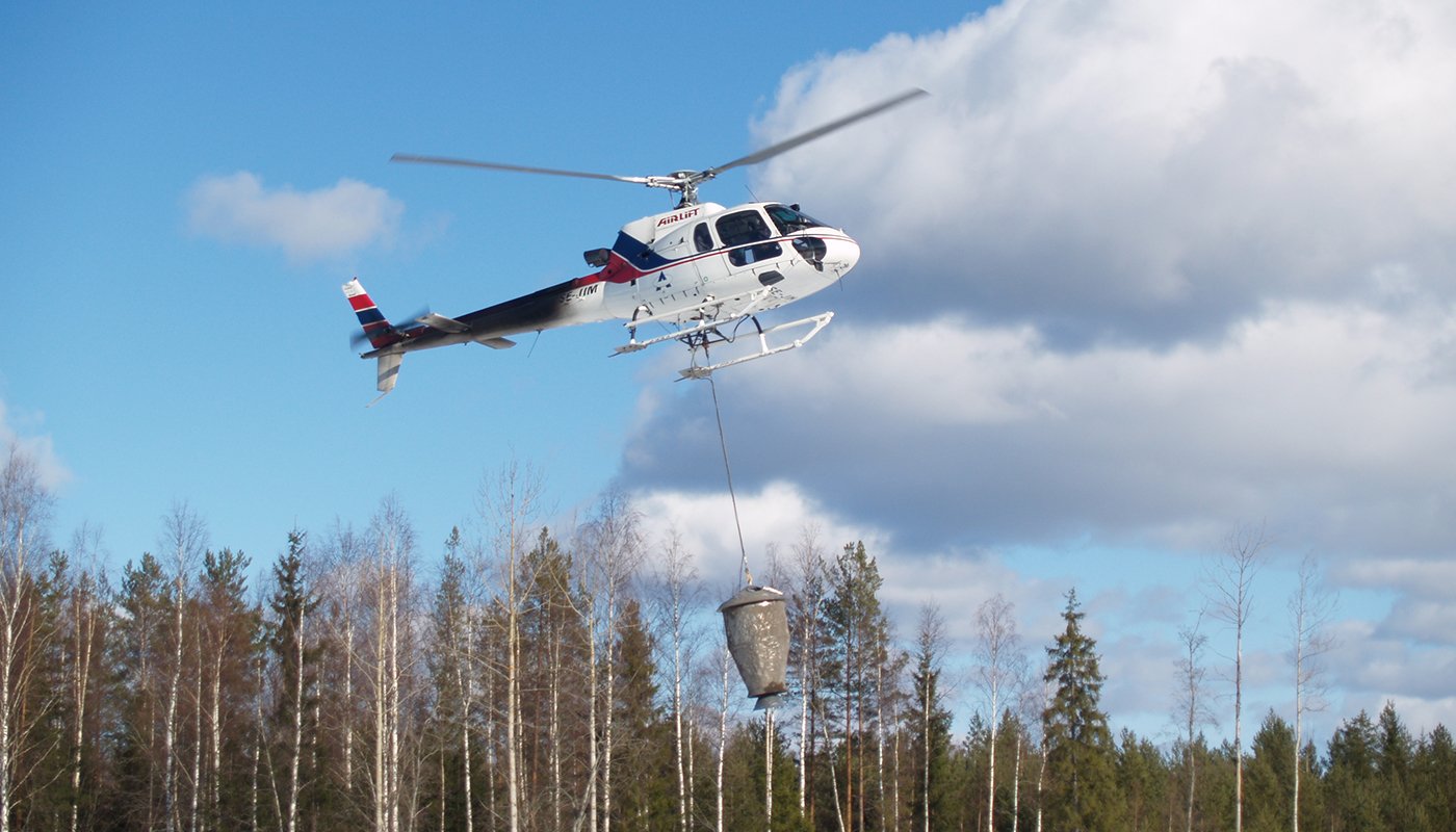 Helikopteri levittää tuhkalannoitetta metsään. 
