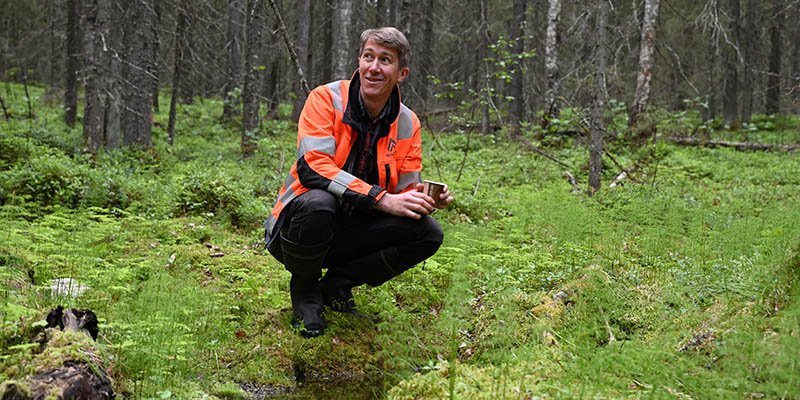 Jussi Vatanen on kyykistyneenä metsässä olevan lähteen vieressä. 