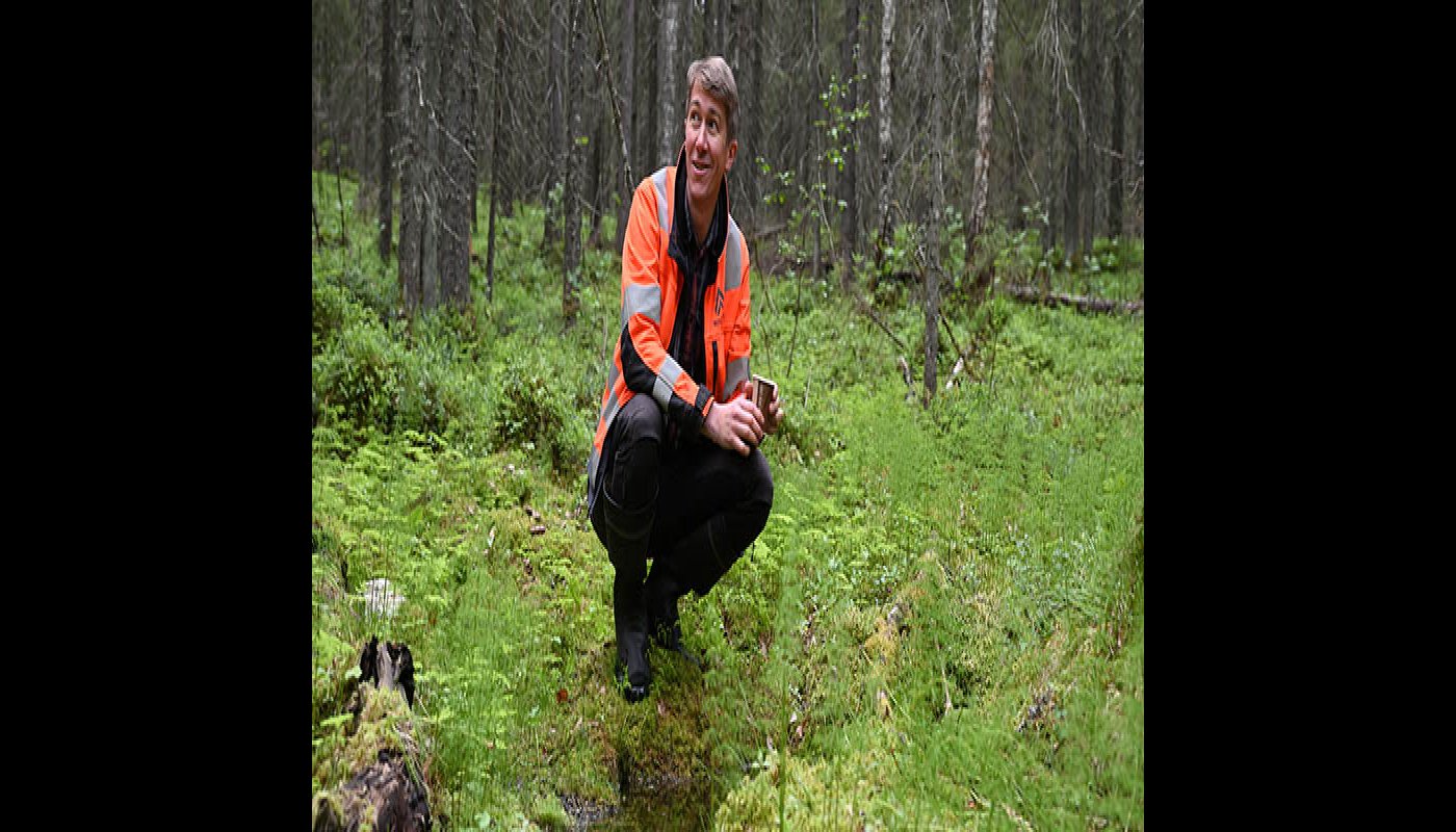 Jussi Vatanen on kyykistyneenä metsässä olevan lähteen vieressä. 
