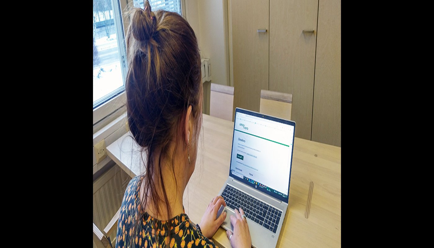 Nainen katsoo kannettavalta tietokoneelta OmaVero-palvelua puisen pöydän ääressä. 