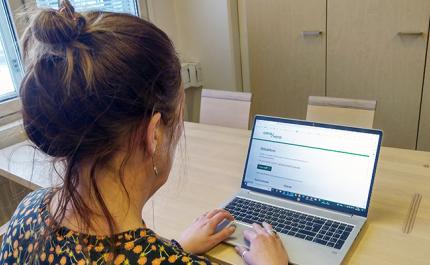 Nainen katsoo kannettavalta tietokoneelta OmaVero-palvelua puisen pöydän ääressä. 