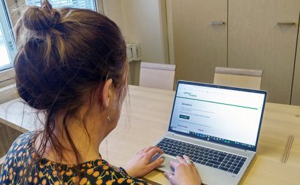 Nainen katsoo kannettavalta tietokoneelta OmaVero-palvelua puisen pöydän ääressä. 