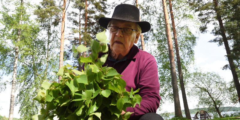 Mies työstää koivunvihtaa ulkona.