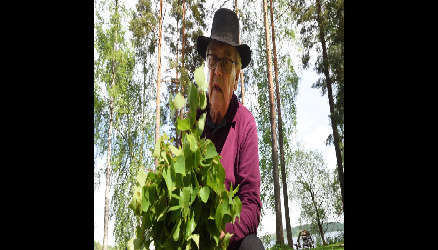 Mies työstää koivunvihtaa ulkona. 