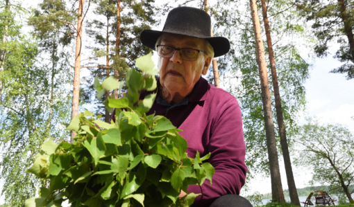 Mies työstää koivunvihtaa ulkona.