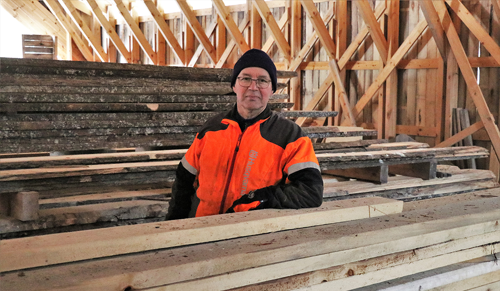 Jarmo Sirola seisoo sahattujen lautapinojen välissä varastorakennuksessa.