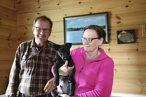 Hirsisen loma-asunnon omistajat Reino Ronkainen ja Hilkka Ronkainen sylissään Remy-koira. 