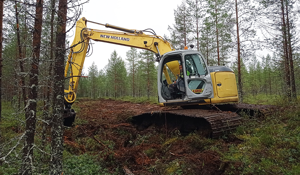 Kaivinkone on tukkimassa ojaa suometsässä. 