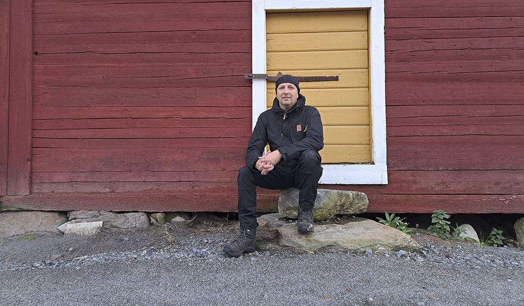 Marko Ämmälä istuu punaseinäisen hirsirakennuksen kivirappusilla.
