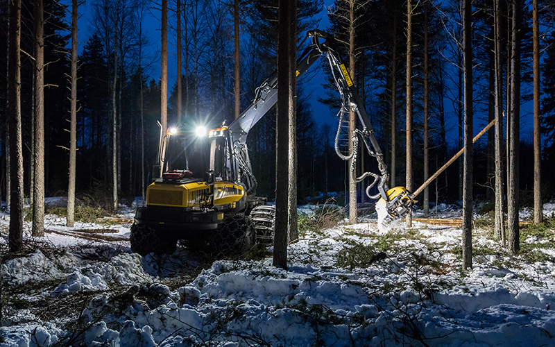 Hakkuukone harventaa metsää talvella iltahämärässä. 