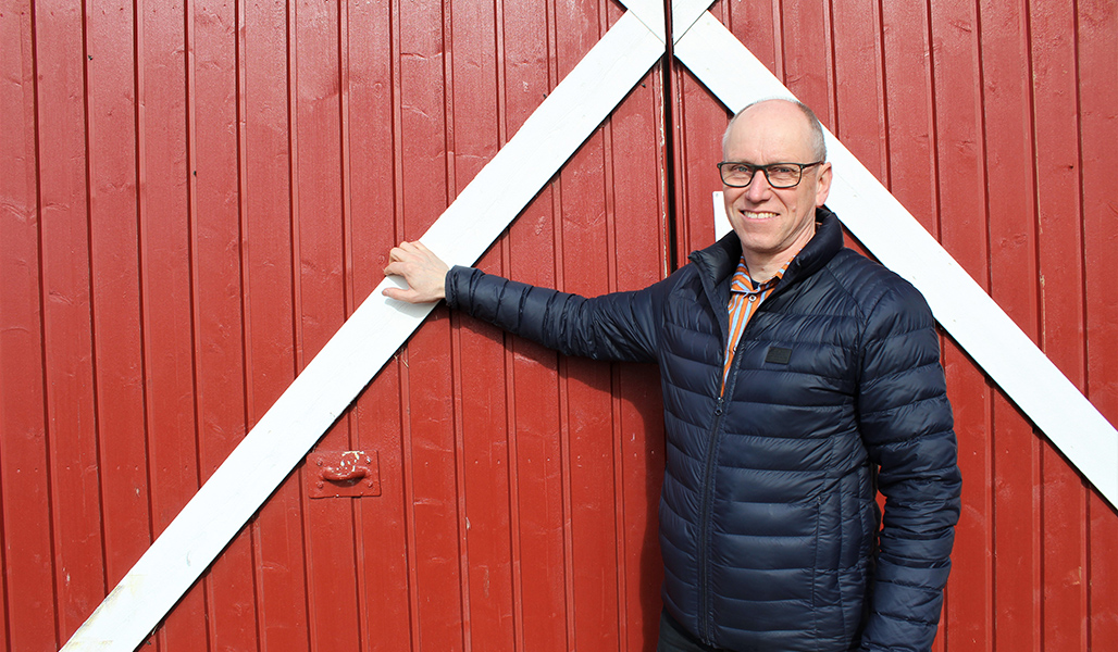 Martti Kangasniemi seisoo punaisen puumaneesirakennuksen vieressä.