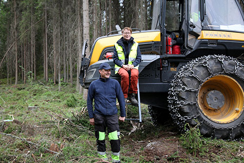 Metsäkoneenkuljettaja Kyösti Karhila ja Teija Hyytiäinen-Koskimäki metsäkoneen edessä hakkuutyömaalla. 