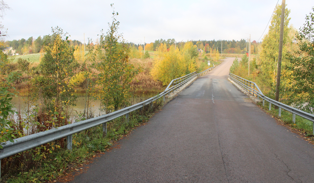 Kuvassa on asvaltoitu yksityistie ja silta, joka ylittää joen. Ympärillä on syksyistä maaseutumaisemaa.