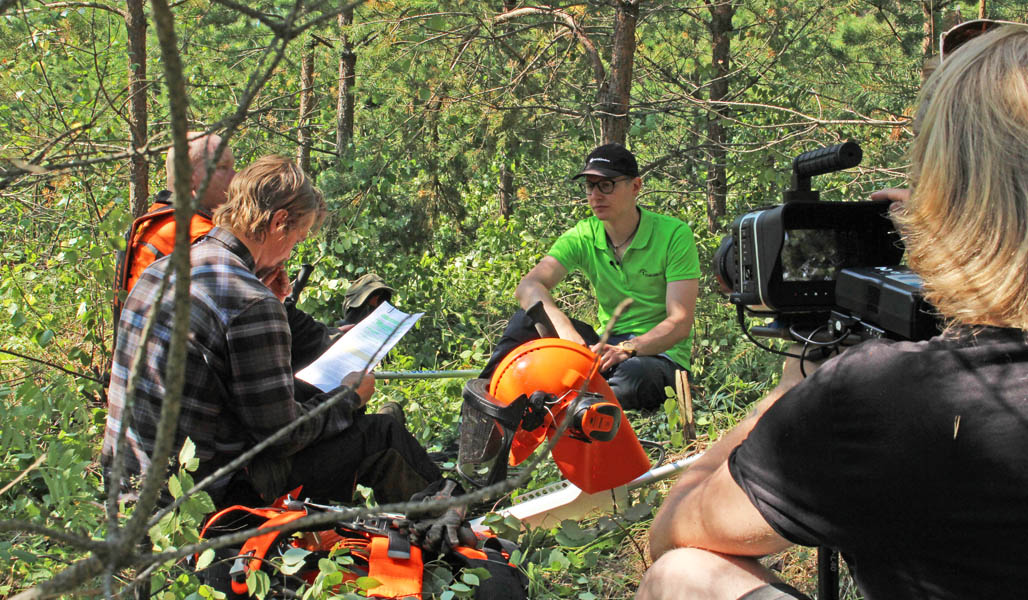 Roope Tonteri, metsuri Ari Oinas ja metsäneuvoja Henri Hiltunen kuvaustauolla metsässä. Oikealla kuvassa on videokamera ja kuvaaja. 