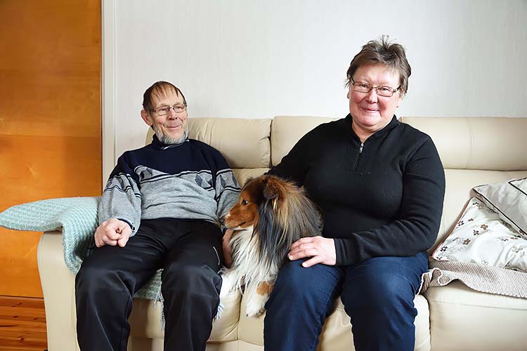Auvo ja Helena Alanne omalla kotisohvallaan. Heidän keskellään istuu Roope-koira. 